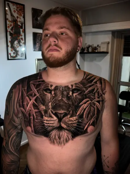 Tatuaje black and grey de pecho completo: rostro de león realista entre hojas de bambú, con la palabra “Fe” en la frente, Buenos Aires