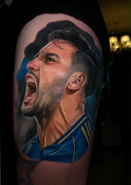 Tatuaje realista a color de futbolista gritando un gol con camiseta azul y oro, retrato de perfil en el brazo, hecho en Recoleta, Buenos Aires