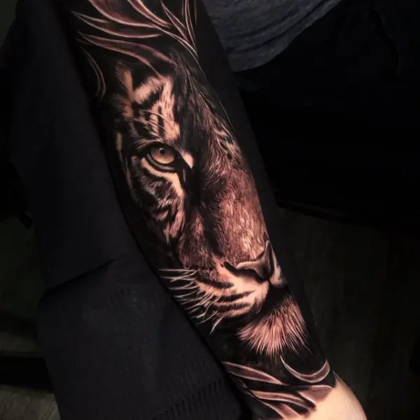 Tatuaje realista black and grey de medio rostro de tigre con ojo ámbar entre hojas, en el antebrazo, hecho en Recoleta, Buenos Aires