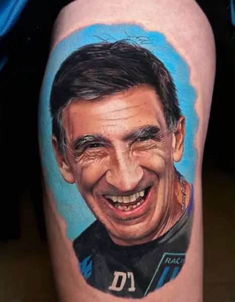 Tatuaje realista a color de retrato sonriente con camiseta de Racing Club sobre fondo celeste, en el muslo, hecho en Recoleta